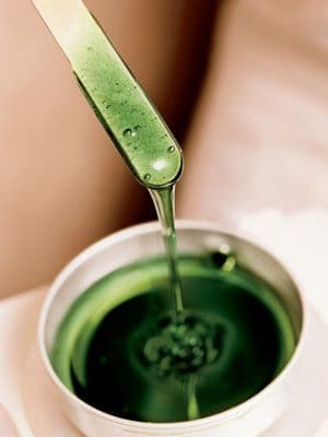 Green wax pot and spatula on a work surface.