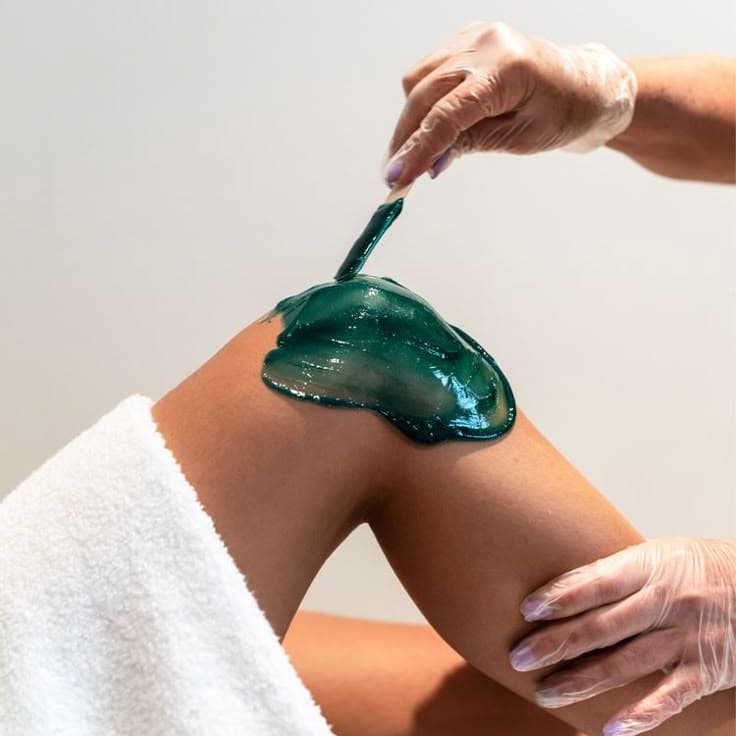 Gloved therapist applying green wax to a person's leg.