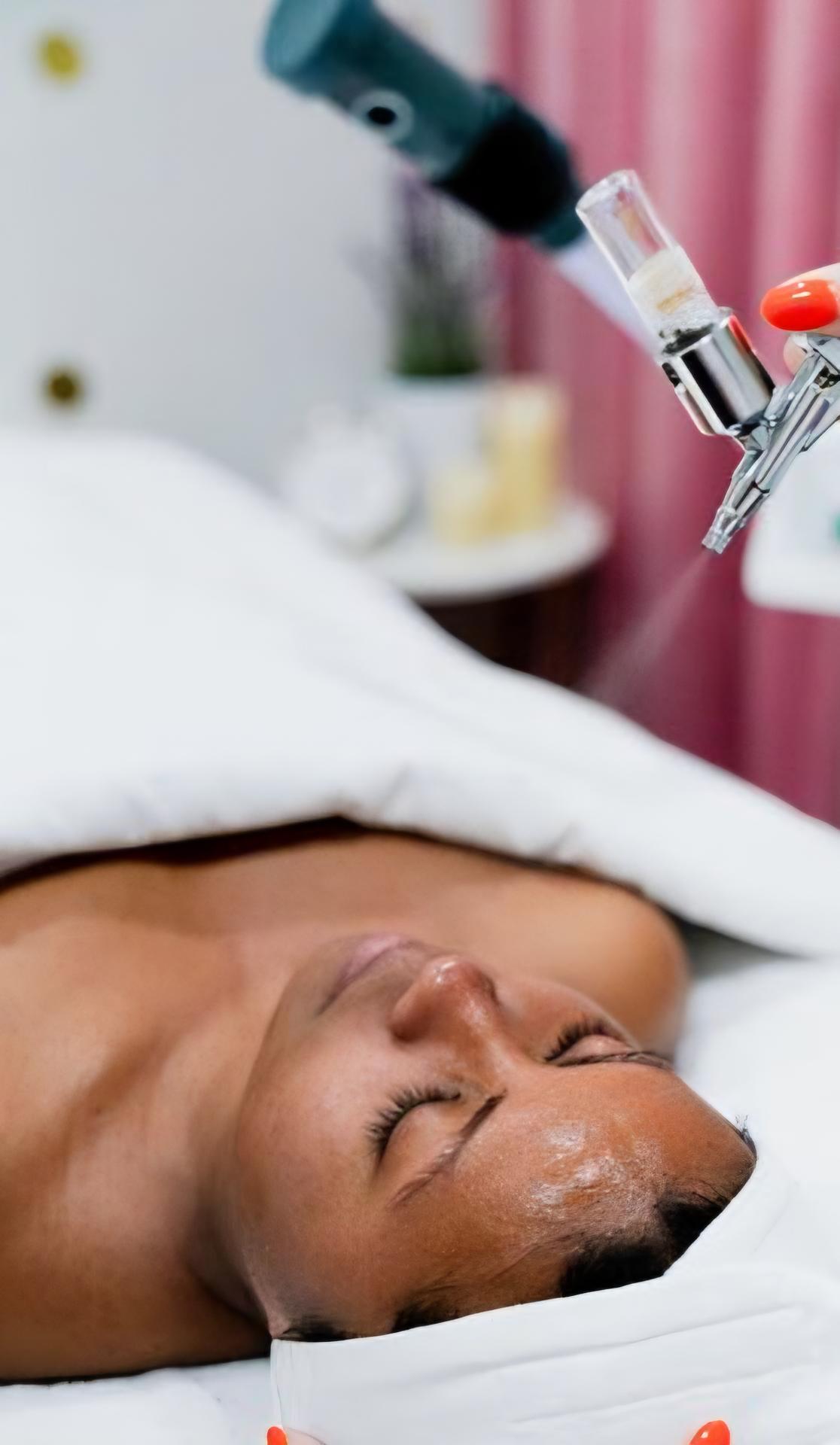 Person receiving a facial treatment with a handheld spray device.