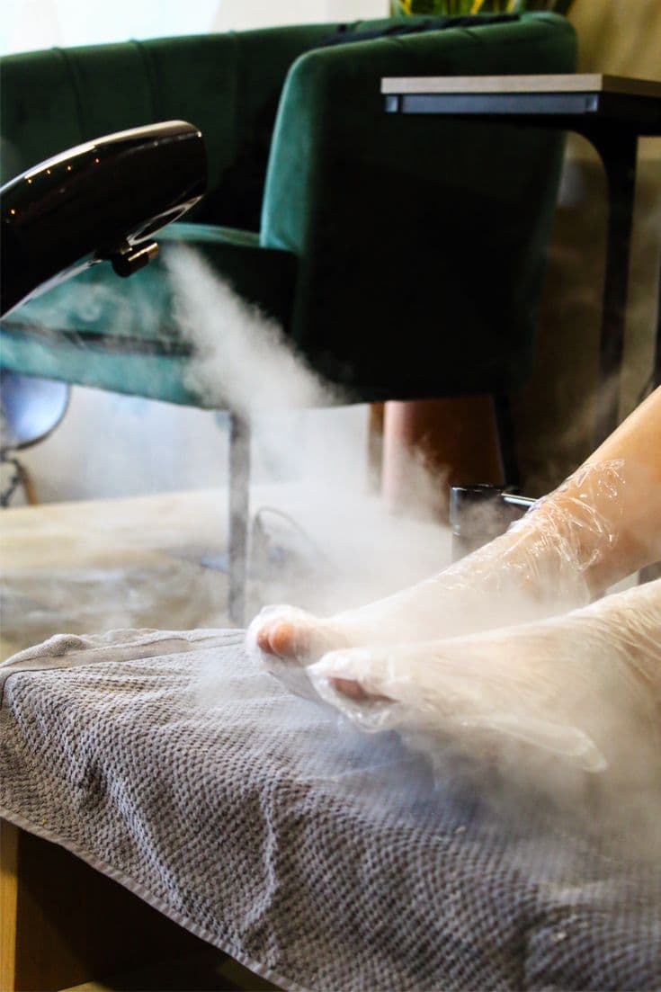 Feet wrapped in film under a pedicure steamer.
