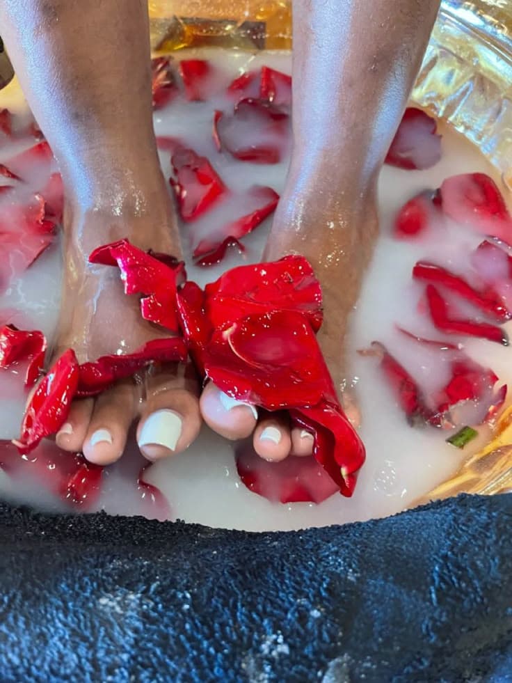 Feet soaking in milky water with rose petals.